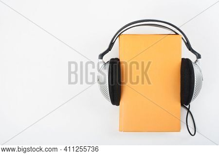 Audiobook On White Background. Headphones Put Over Yellow Hardback Book, Empty Cover, Copy Space For