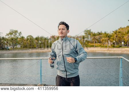 Young Sport Man Hold Water Bottle Between Jogging And Listening Music In The Park.