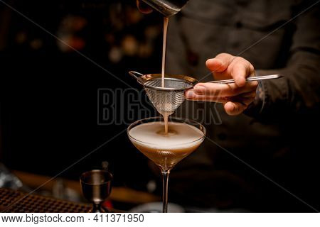 Close-up On Sieve Through Which Male Bartender Pours Frothy Espresso Martini Cocktail Into Glass