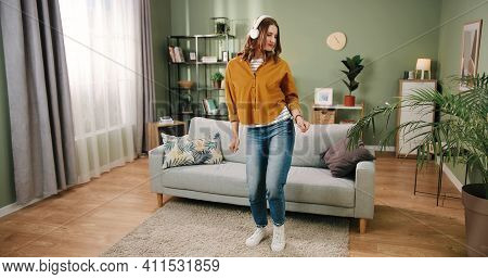 Caucasian Young Beautiful Joyful Woman Dancing In Modern Living Room In House Alone Listening To Mus