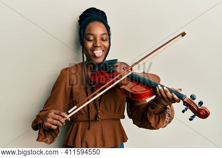 African american woman with braided hair playing violin sticking tongue out happy with funny expression. 
