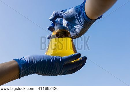 Hand With Gloves Holding Beaker With Ethanol Biofuel Against Blue Sky