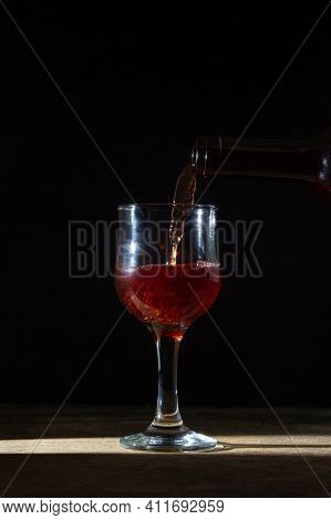 Homemade Red Wine Is Poured Into A Glass On A Dark Background. Glass Of Red Wine On A Black Backgrou