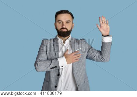 Portrait Of Serious Young Congressman Taking Oath On Blue Studio Background. Trustworthy Deputy Or M