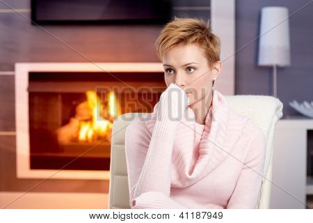 Atraktivní mladá žena sedí doma u krbu v růžový svetr, myšlení.