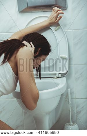 Woman vomits in to the toilet in the bathroom. Young woman vomiting into the toilet bowl in the early stages of pregnancy or after a night of partying and drinking.