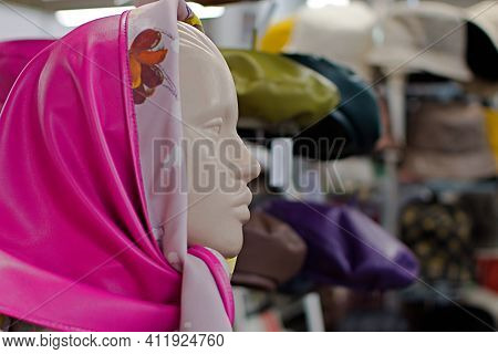Fashion Still Life. Mannequin Head In Bright Pink Leather Scarf On Blurred Background Of Headwares
