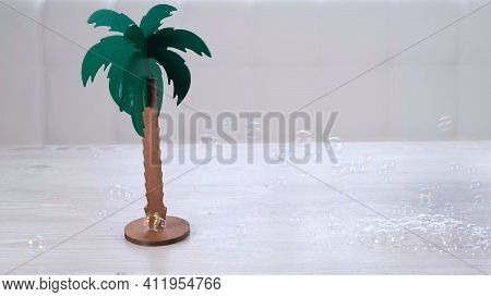 Rtificial Palm Tree And Rainbow Soap Bubbles On A White Wooden Table. Relaxation And Imagination Con