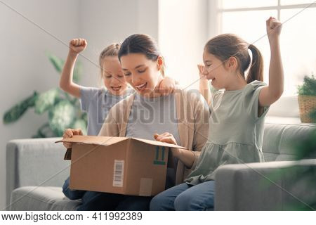 Mother and daughters are unpacking cardboard box at home.