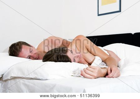 Young couple sleeping in  late in a hotel bed, the man's hand wrapped around his girlfriends waist