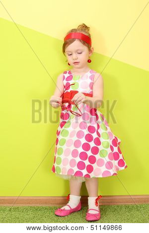 A little girl in a bright varicolored dress holding a rim of glasses