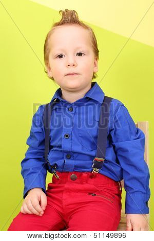 Mod boy in bright clothes sits on a background yellow and green wall