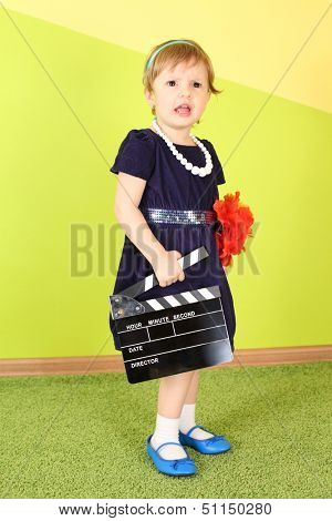Little girl in a dark blue dress holds a clapstick in her hand