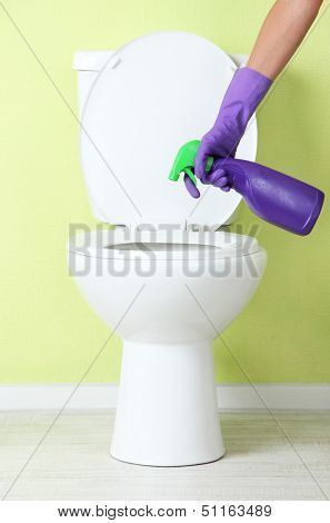 Woman hand with spray bottle cleaning a toilet bowl in a bathroom