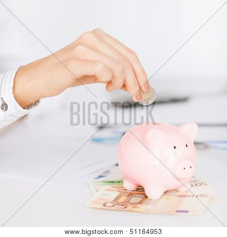 business, office, household, school, tax and education concept - woman hand putting coin into small piggy bank