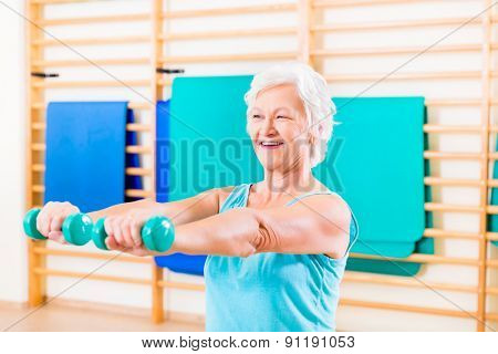 Senior woman doing fitness sport in gym with dumbbells