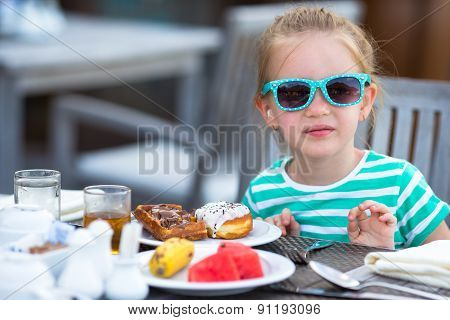 Adorable little girl having breakfast at outdoor cafe