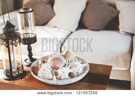 Beach interior decor: sea shells and lanterns on the wooden coffee table, natural colors. Detail of living room.