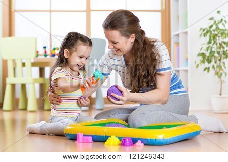 Child little girl and mother playing with kinetic sand at home
