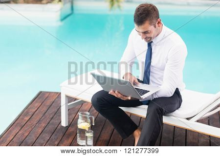 Smarty dressed using laptop near poolside while sitting on sun lounger