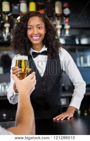 Beautiful barmaid serving glass of beer to man at bar counter in bar