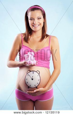 개념적 이미지와 함께 행복 한 임신 여성의 손에 그녀의 아랫 배와 아기의 옷에 시계 그린