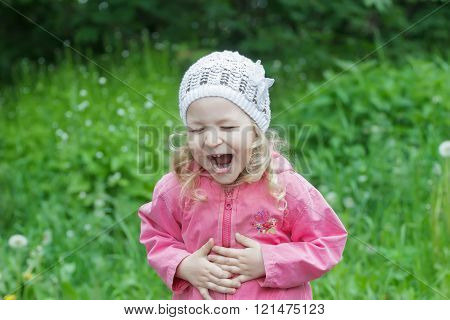 Little Caucasian girl bending with belly laughter in spring green garden