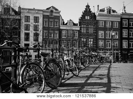 AMSTERDAM NETHERLANDS - 16TH FEBRUARY 2016: Lots of bikes chained to the railings of a bridge in Amsterdam. Typical Amsterdam style buildings can be seen in the background.