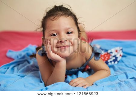 smiling latino girl laying on blye blanket bed