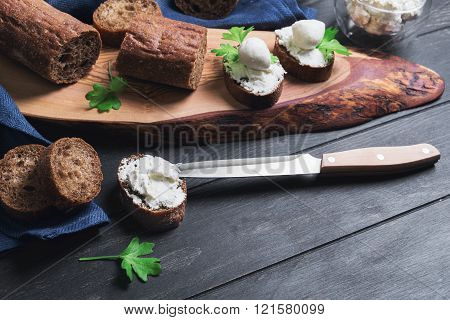 On a dark black wooden background small sandwiches canape bagget rye bread mozzarella Philadelphia cheese celery knife