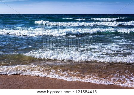 Blue Fresh Water Whitecap Waves Wash Ashore onto a Sandy Beach. Rhythm of Nature. Bright Clear Day. Seashore Background with Copy Space.