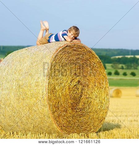 Little kid boy sitting on hay bale in summer