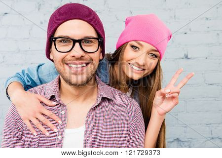 Cheerful Girl Embracing Her Boyfriend And Gesturing With Two Fingers