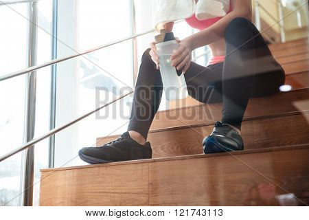 Closeup of attractive sportswoman sitting and drinking water