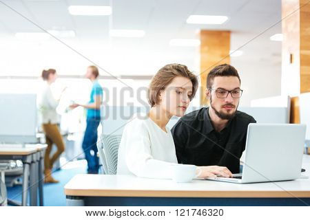 Serious focused young man and woman sitting and working with laptop together in office