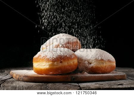 Donuts sprinkled with powdered sugar on wooden table on black background closeup. Food background
