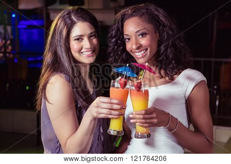 Young women toasting cocktail glasses at bar counter in bar