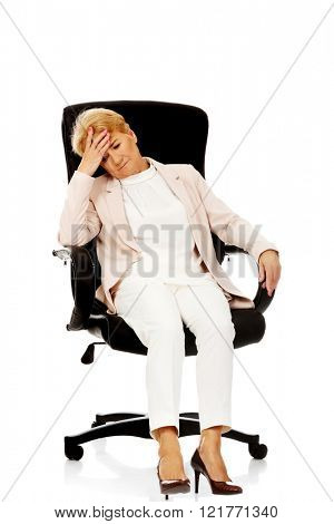 Worried elderly business woman sitting on armchair