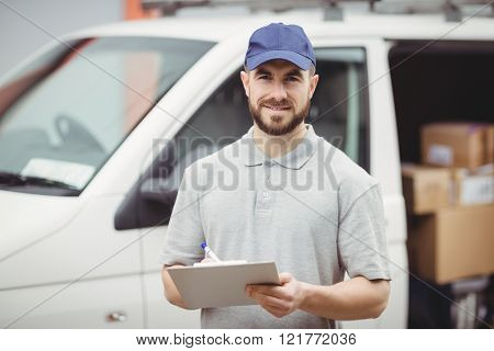 Delivery man writing on clipboard in front of his van