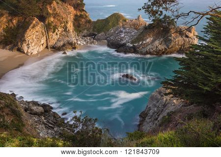 Waterfall in Julia Pfeifer Burns State Park at sunset with a soft golden color on the rocks