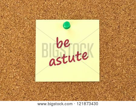The phrase Be Astute in red text on a yellow sticky note posted to a cork notice board.