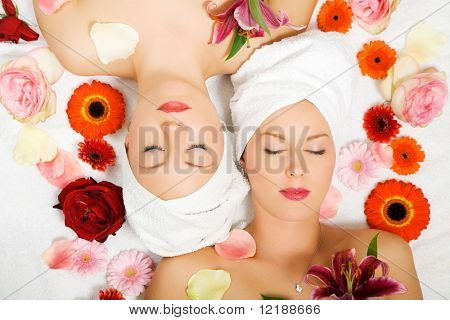 To piger afslappende i en wellness set-up set fra oven, justeret lodret, med masser af blomster, c