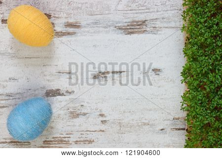 Easter eggs wrapped woolen string and green cuckooflower cress on old wooden background, copy space for inscription or text, decoration for Easter