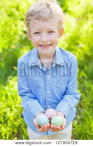 cheerful little boy holding three colorful easter eggs after egg hunt in the park