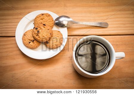 White cup of coffee with chocalate chips cookies in white dish focus at edge of coffee cup