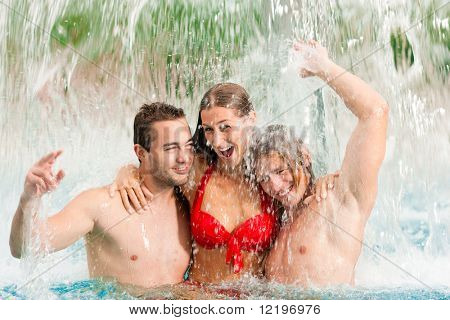 Three young people - woman and two men - at a public swimming pool standing under a water gadget