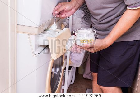 Person adding baking soda into washing machine to wash clothes for brighter and cleaner finish