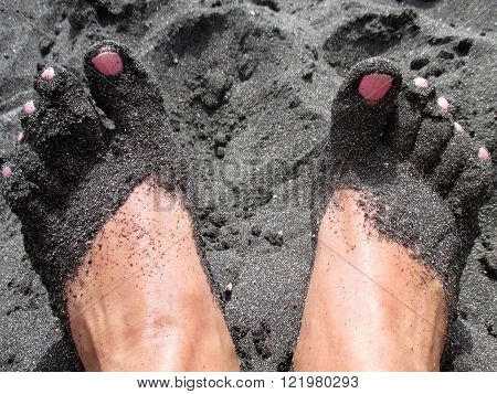 feet with black sand on a volcanic beach