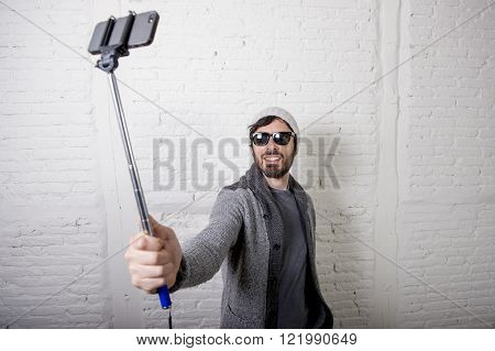 young attractive man in casual clothes beanie hipster style holding selfie stick mobile phone shooting self portrait photo or recording video in internet blog and blogger concept
