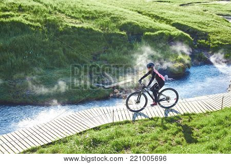 woman cyclist bikes down the slope in the Valley of the river of Hveragerdi Iceland. Hiking Tour of Reykjadalur Hot Springs